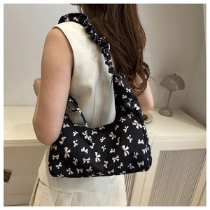 Close-up of black canvas shoulder bag with white bow patterns and pleated strap details