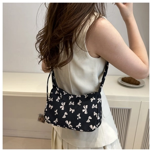 Detail of black underarm bag with pink bow pattern shown on model in minimalist setting