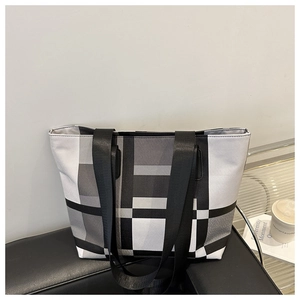 Détail d'un grand sac cabas à carreaux avec de larges anses sur un fauteuil en cuir