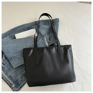 Vista piatta di una borsa tote nera su lenzuola bianche con giacca di jeans e libro