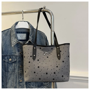 Dettaglio della borsa tote grigia con stelle e fiocco in metallo su giacca di jeans