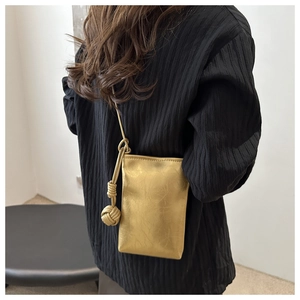 Mini sac bandoulière doré texturé avec pompon porté par un mannequin en gros plan