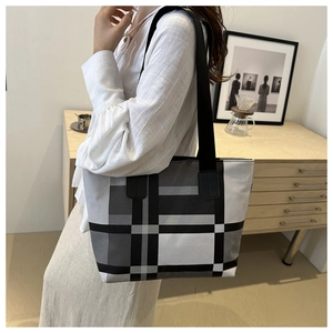 Détail du grand sac cabas à carreaux avec anses noires porté par un mannequin en décor épuré
