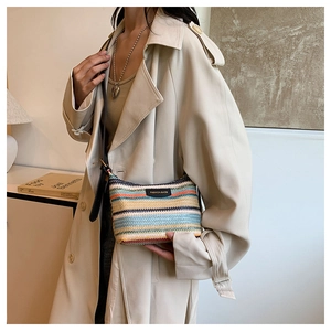 Detail of colorful striped woven shoulder bag with black leather strap on a model