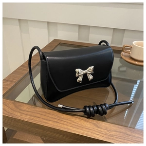 Détail du sac baguette noir minimaliste avec boucle noeud argentée et bandoulière à noeuds
