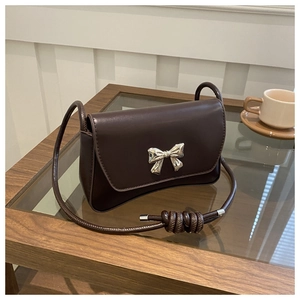 Détail d'un sac bandoulière en cuir marron avec boucle nœud en métal argenté et bandoulière