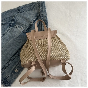 Dettaglio di uno zaino in paglia intrecciata con spallacci in pelle beige su fondo denim