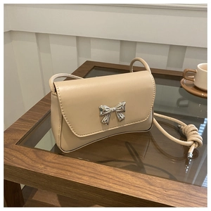 Gros plan sur un sac à rabat beige en similicuir avec un nœud en métal argenté