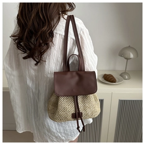 Detail view of woven straw backpack with leather flap and drawstring closure on a model