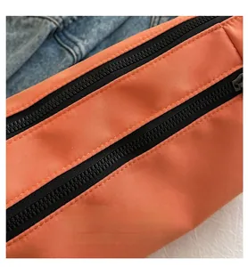 Detail of orange nylon bag featuring dual black zippers and fine stitching texture