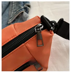 Detailed close-up of smooth black zipper and metal puller on an orange crossbody bag