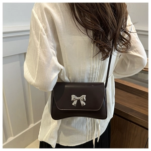 Gros plan d'un sac bandoulière marron café avec une boucle en métal en forme de nœud