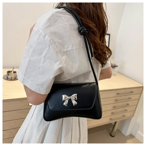 Vue détaillée d'un sac baguette noir mat avec un nœud argenté et une bandoulière en cuir