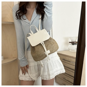 Detailed view of bohemian woven straw and white leather backpack on model indoors