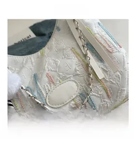 Detailed texture of white embossed fabric with colorful floral embroidery and chain strap