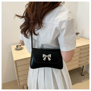 Vue arrière d'un sac bandoulière en cuir noir avec nœud argenté sur une robe à rayures