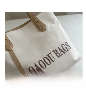 Detail of canvas tote bag showing brown leather handles with reinforced stitching