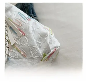 Close-up of white embossed canvas tote with colorful embroidery and metal chain strap