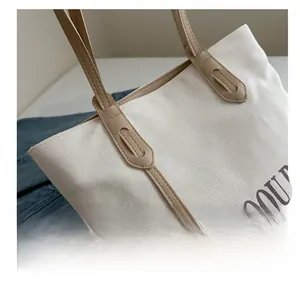 Close-up of contrast stitching on canvas tote bag with khaki leather shoulder strap detail