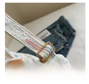 Close-up of white woven bag strap with golden buckle and colorful stitching details