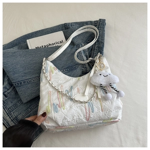 Detail of white quilted tote bag with colorful embroidery and plush cloud charm