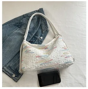 Detail of white quilted tote bag with wave embroidery and smartphone for size comparison