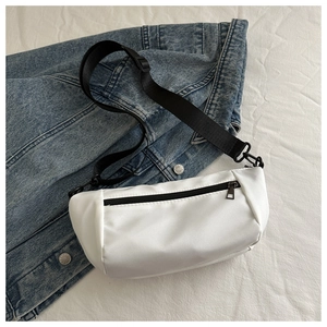 Close-up of a white waterproof nylon crossbody bag with black zippers on denim jacket