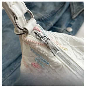 Detail of silver metal zipper on white textured shoulder bag with color embroidery