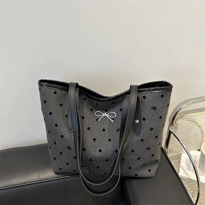 Borsa tote grigia a pois con fiocco in argento su panca in pelle in un ambiente moderno