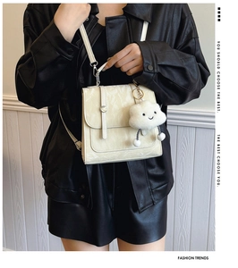Detail van crèmewitte crossbodytas met marmertextuur en pluche wolkbedeltje op lederen jas