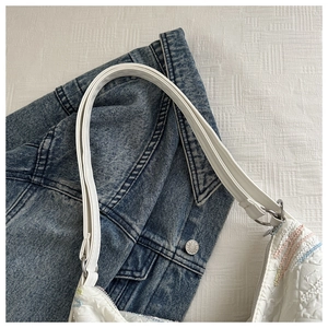 Close-up of white textured handbag featuring colorful wavy embroidery and silver metal rings
