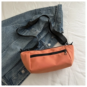 Detail of coral orange nylon crossbody bag on denim jacket showing texture and zipper