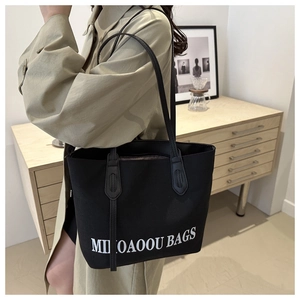 Close-up of black tote bag with white text print on a woman in a green trench coat