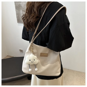 Detail of beige textured tote bag with leather straps and a plush cloud charm accessory