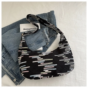 Detail of hobo bag with colorful wave embroidery and wide strap on white textured fabric