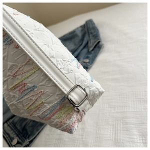 Detail of white nylon bag featuring colorful wavy embroidery and silver metal buckles