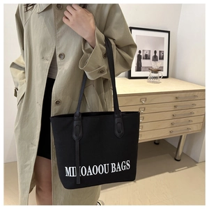 Detail of the black canvas tote bag showing the white logo and leather straps on a shoulder