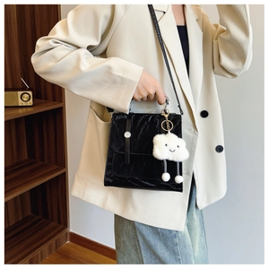 Detail van zwarte crossbodytas met metalen gesp en pluche wolkje als accessoire