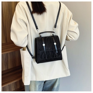 Detail of a black pleated backpack with silver buckles worn with a cream blazer
