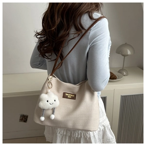 Detail of beige waffle-texture tote bag with brown leather strap and plush cloud charm
