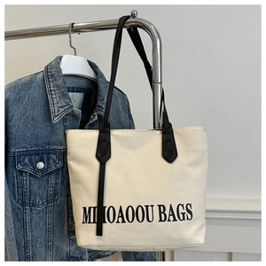Détail du sac cabas en toile blanc cassé avec imprimé noir suspendu à un cintre en métal
