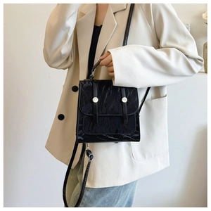 Detail of black pleated patent leather bag with silver metal buckles on a model