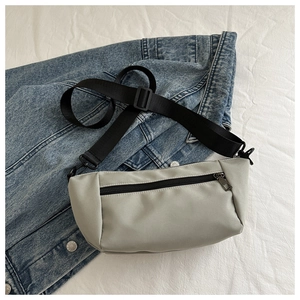 Detail view of light grey nylon waist bag on denim jacket with adjustable black strap