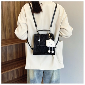 Detail of a black textured mini backpack with a white plush cloud charm for a modern look