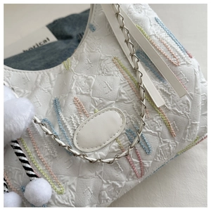 Detail of white canvas tote featuring colorful embroidery, metal chain and pompom