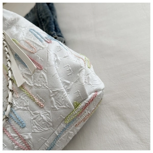 Detail of white quilted canvas tote with colorful embroidery and metal chain strap