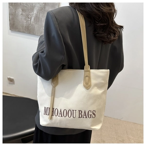 Détail d'un sac cabas en toile beige avec anses marron porté par une femme à l'épaule