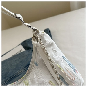 Close-up of white embossed tote bag with colorful embroidery and metal chain strap