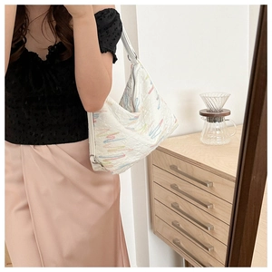 Detail of white quilted tote with colorful embroidery shown in a modern lifestyle setting