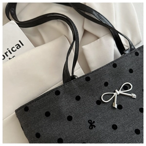 Close-up of black textured tote bag with 3D polka dots and silver metal bow charm
